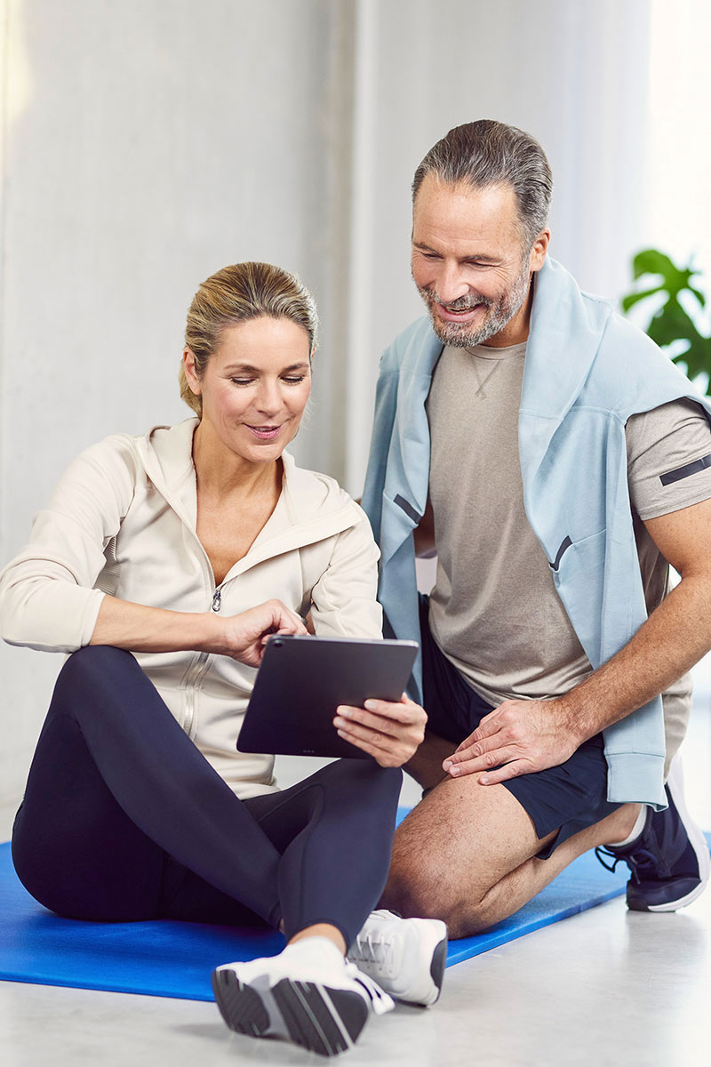 Mann & Frau bedienen ein Tablet und sind im Trainingsoutfit
